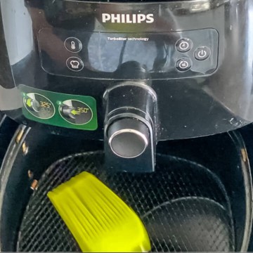 A brush coating the air fryer basket with oil.