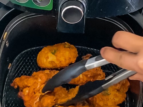 Tongs flipping the chicken in the air fryer basket