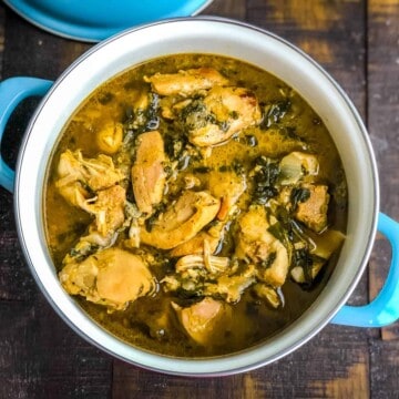 A blue handled bowl with methi chicken on a wooden counter.