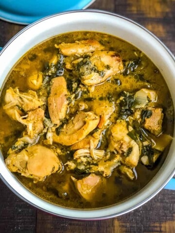 A blue handled bowl with methi chicken on a wooden counter.