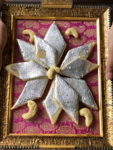 A hand holding a plate of Kaju barfi