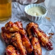 A stack of BBQ chicken wings on a piece of parchment paper with a small cup of ranch in the back with the words 30 Minute Air Fryer BBQ Chicken Wings at the top.
