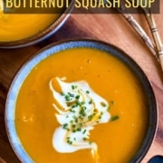 A blue bowl of butternut squash soup with coconut milk and chive in the middle on an orange placemat with two spoons in the top right and the words 30-minute butternut squash soup at the top.
