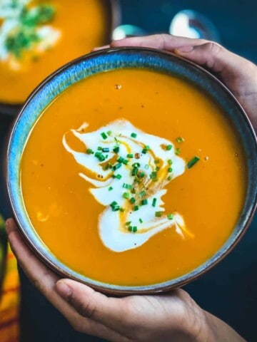 A square photo of Instant pot butternut squash soup in a blue bowl being held by two hands.