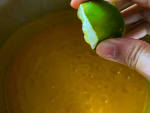 A hand squeezing lime juice into the butternut squash soup.