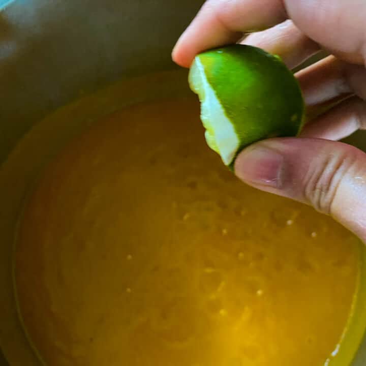 A hand squeezing lime juice into the butternut squash soup.