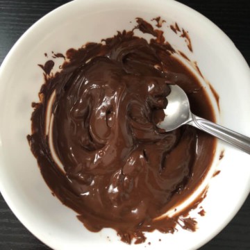 A white bowl with melted chocolate being stirred by a spoon.