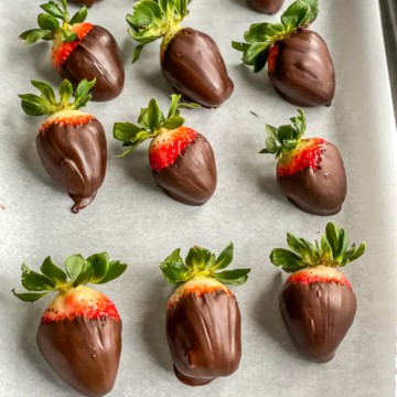 A parchment paper lined baking sheet with chocolate dipped strawberries cooling.