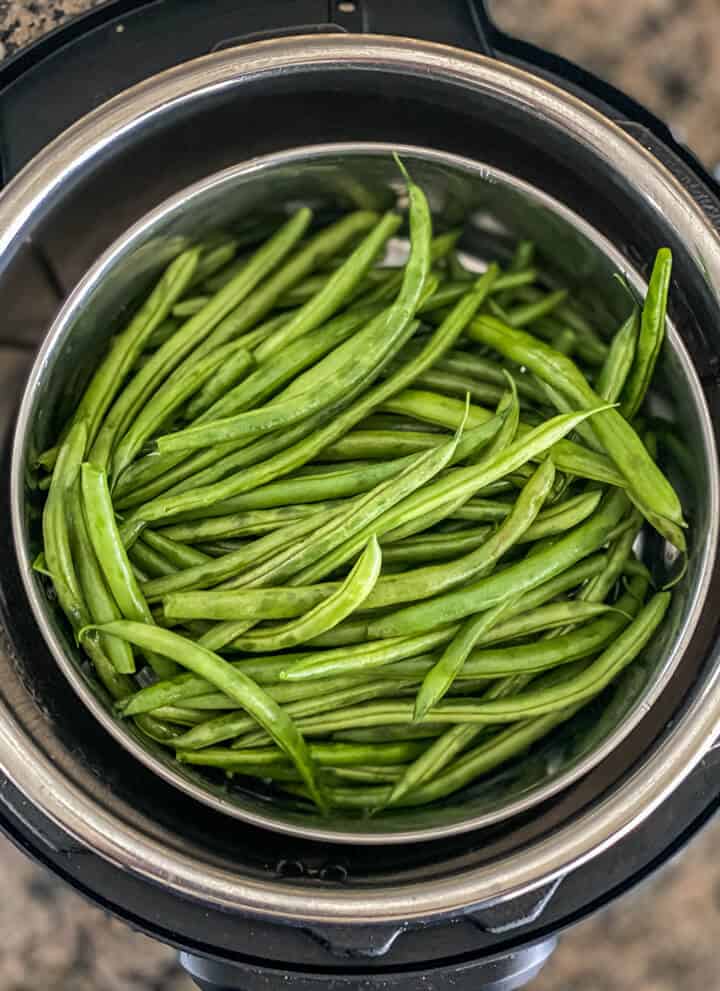 An instant pot with green beans in a steamer basket.