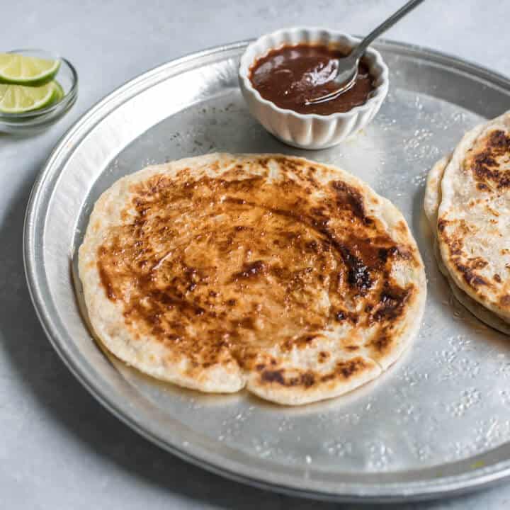 A silver plate with paratha topped with chutney.