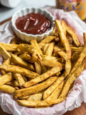 A basket covered in parchment paper with sweet potato fries and a small white bowl of ketchup.