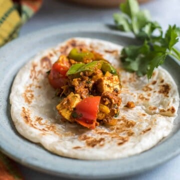 A blue plate with kadai paneer on a paratha with cilantro in the back.