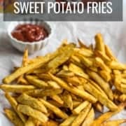 A pile of sweet potato fries with a white bowl filled with ketchup and a bottle of ketchup in the back with the words Air Fryer Sweet Potato Fries at the top.