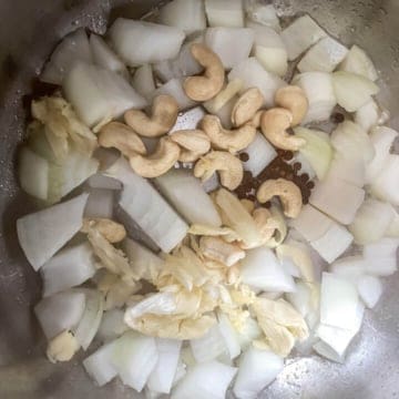 The base of the instant pot with onion, garlic, cashews, and peppercorns.