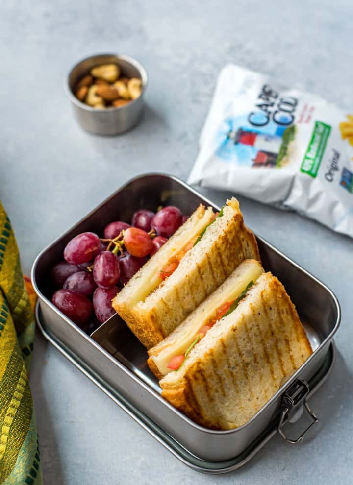 Caprese Sandwich with grapes, chips and mixed nuts on the side.