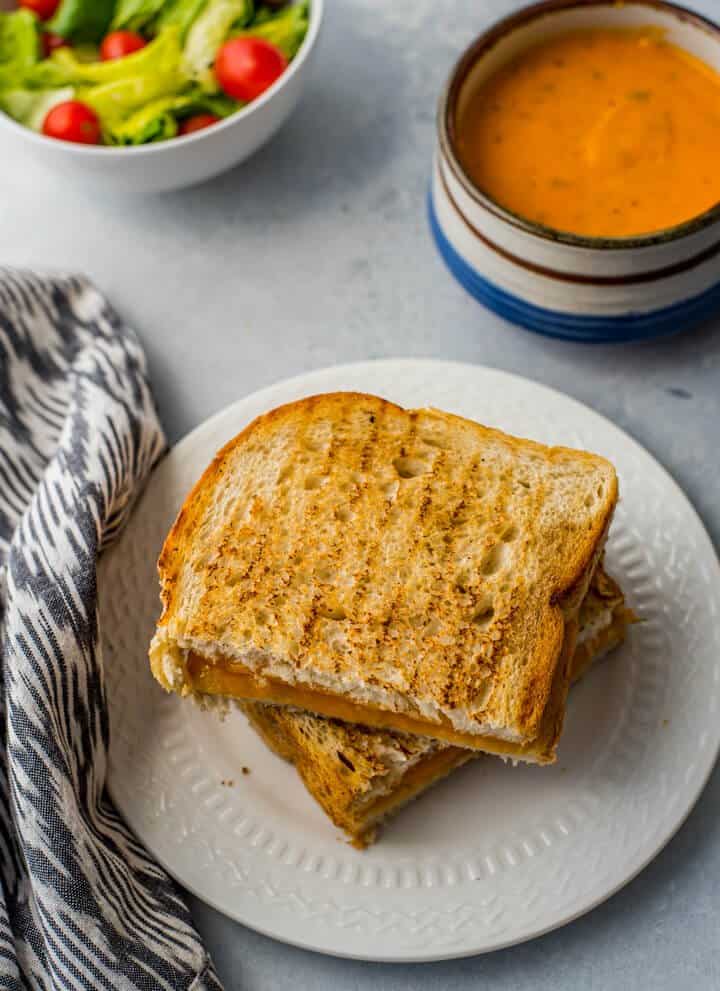 grilled cheese sandwich on white plate with tomato soup