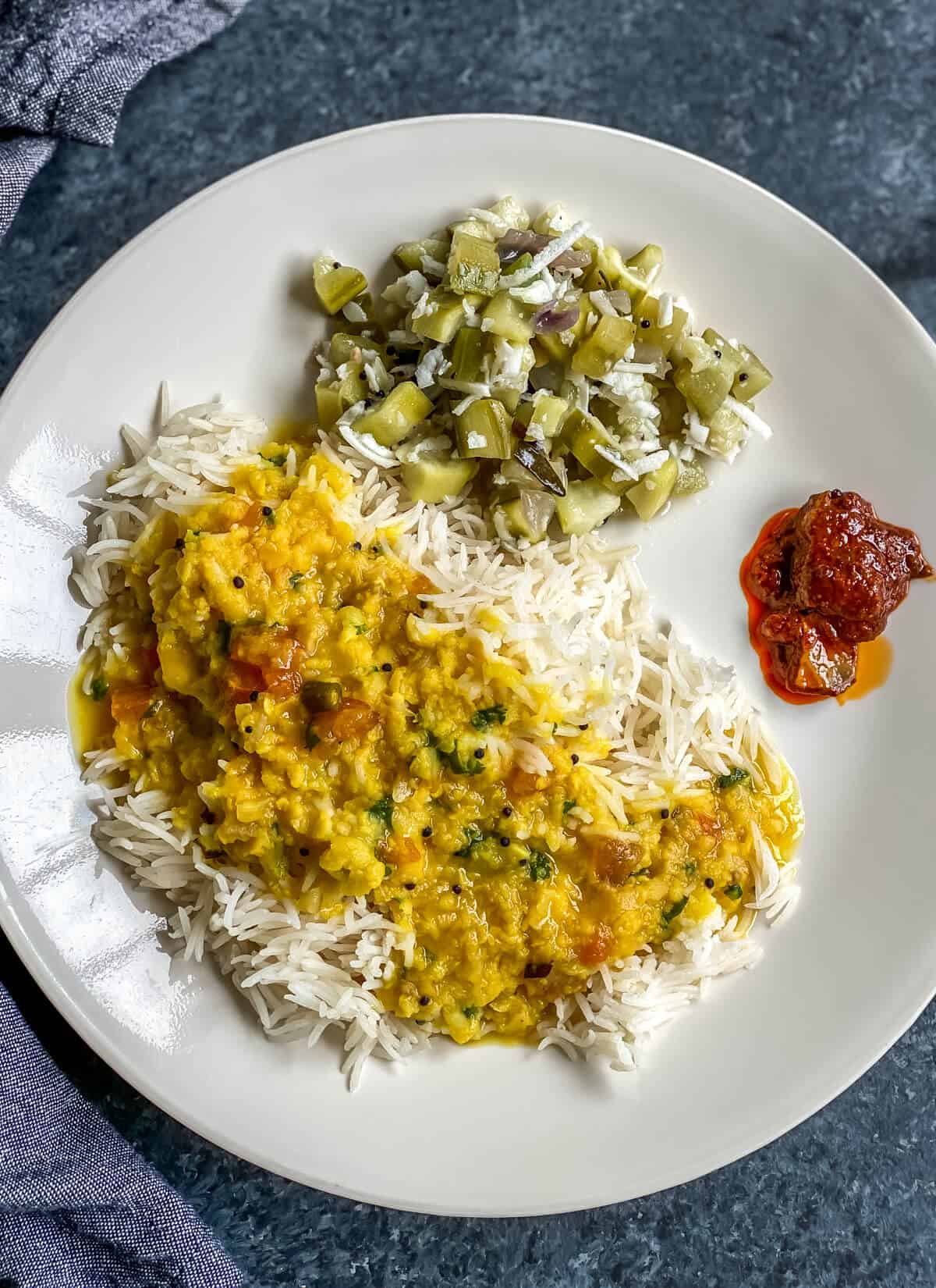 Rice, dal and turiya bhaji served with pickle on a white plate