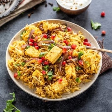 Paneer biryani served in a white bowl with raita