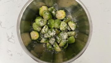 Chopped Brussels sprouts sprinkled with garlic powder and pepper in a steel bowl