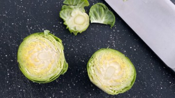 Brussel sprouts chopped into half on a black cutting board