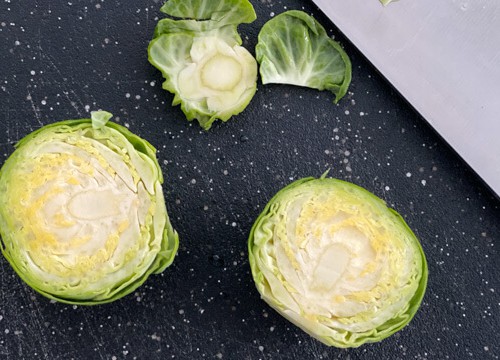 Brussel sprouts chopped into half on a black cutting board