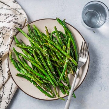 Air Fryer Green Beans (Asian-Style) on a plate with a fork garnished with sesame seeds
