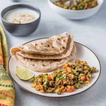 A plate of bhindi masala with a fresh roti on the side, served with a lime wedge.