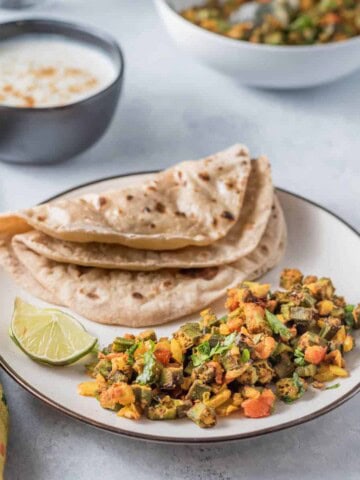 A plate of bhindi masala with a fresh roti on the side, served with a lime wedge.