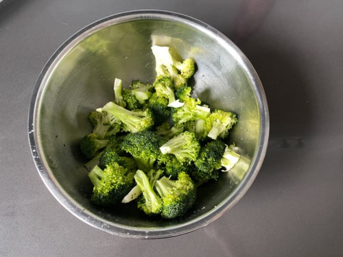 Adding fresh broccoli florets to a bowl of marinade, and tossing to combine.