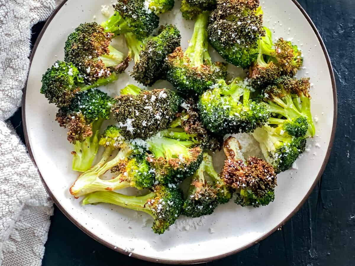 A plate of broccoli that has been roasted in the air fryer, on a dark background.