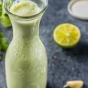 A cruet of cilantro and lime vinaigrette dressing. A lime in the background.