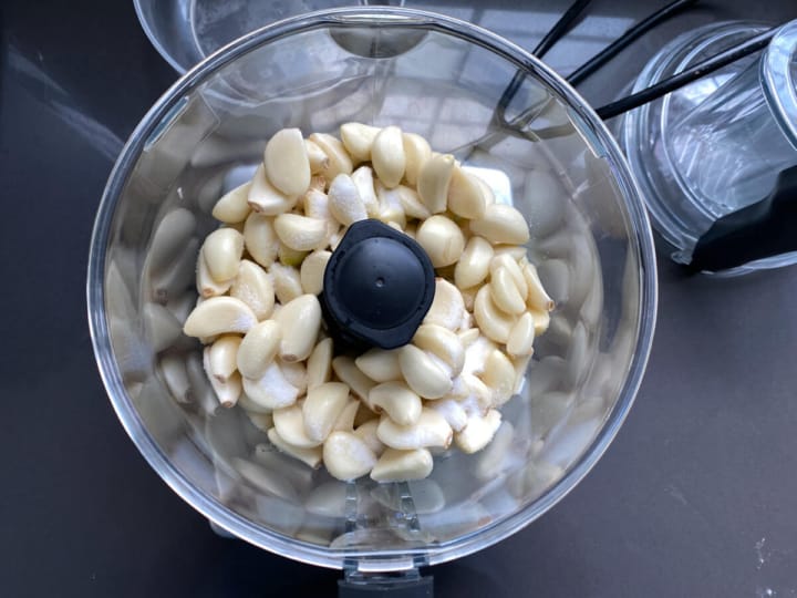 Adding peeled garlic cloves to a food processor.