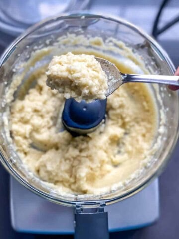 A food processor with garlic paste in it; a spoon lifts out a small portion.