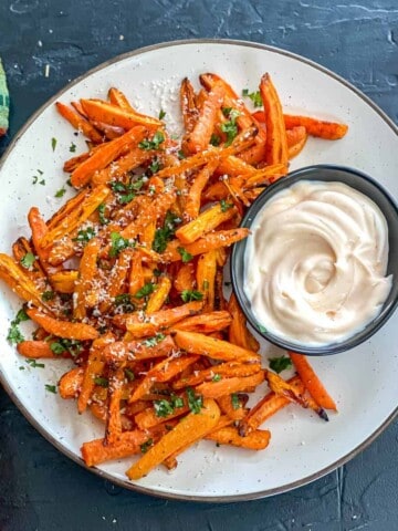 An overheat shot of a plate of roasted carrot fries, with a small bowl of creamy dressing.