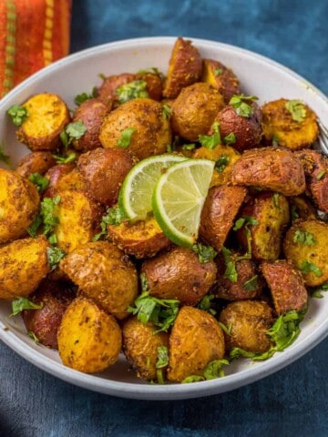 A white bowl of baby potatoes, garnished with parsley and lime wedges.
