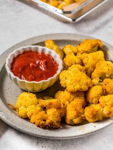 A plate of bright colored cauliflower with a small dish of ketchup on the side.