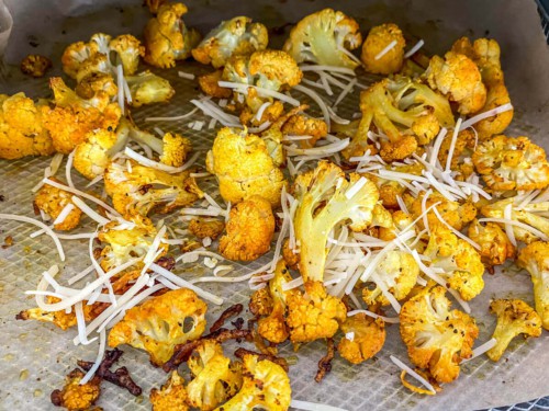 Adding parmesan cheese to a tray of roasted cauliflower.