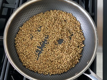A skillet on the stove with coriander seeds.
