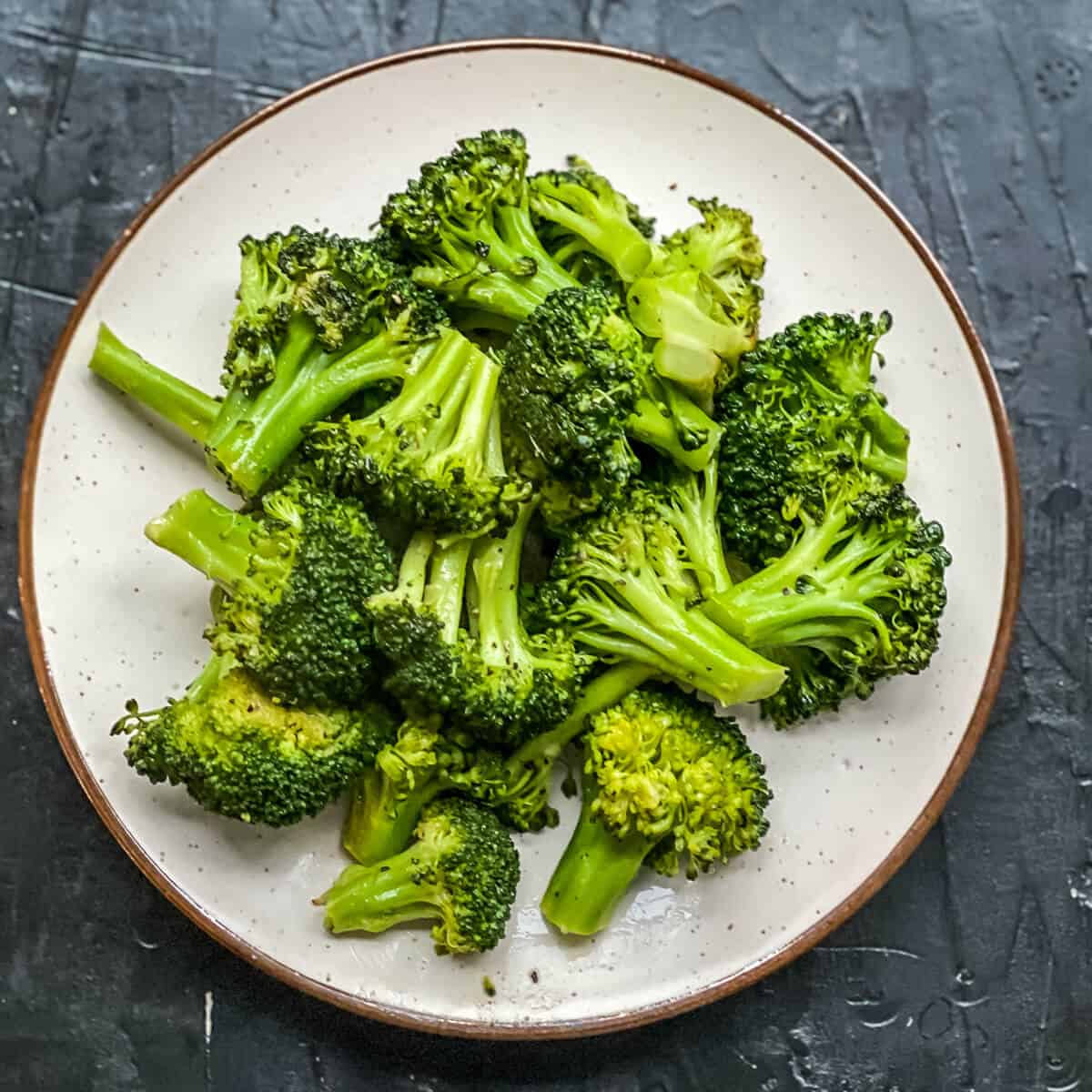 A white plate with a brown rim and bright steamed broccoli in the middle.