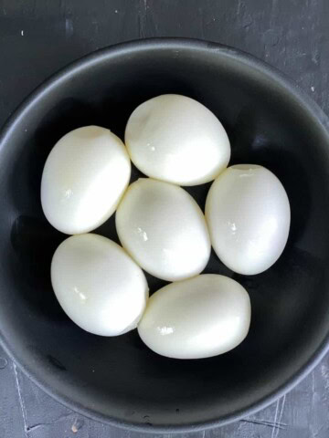 A bowl with six peeled air fryer hard boiled eggs on a grey counter.