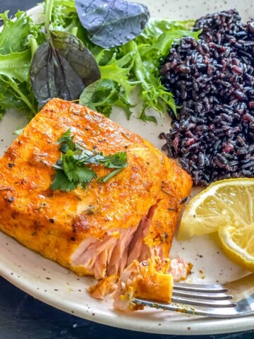 A small portion of salmon, served with black rice and salad.
