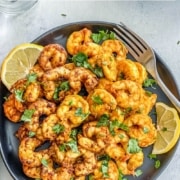 A plate of cooked shrimp, garnished with cilantro and citrus.