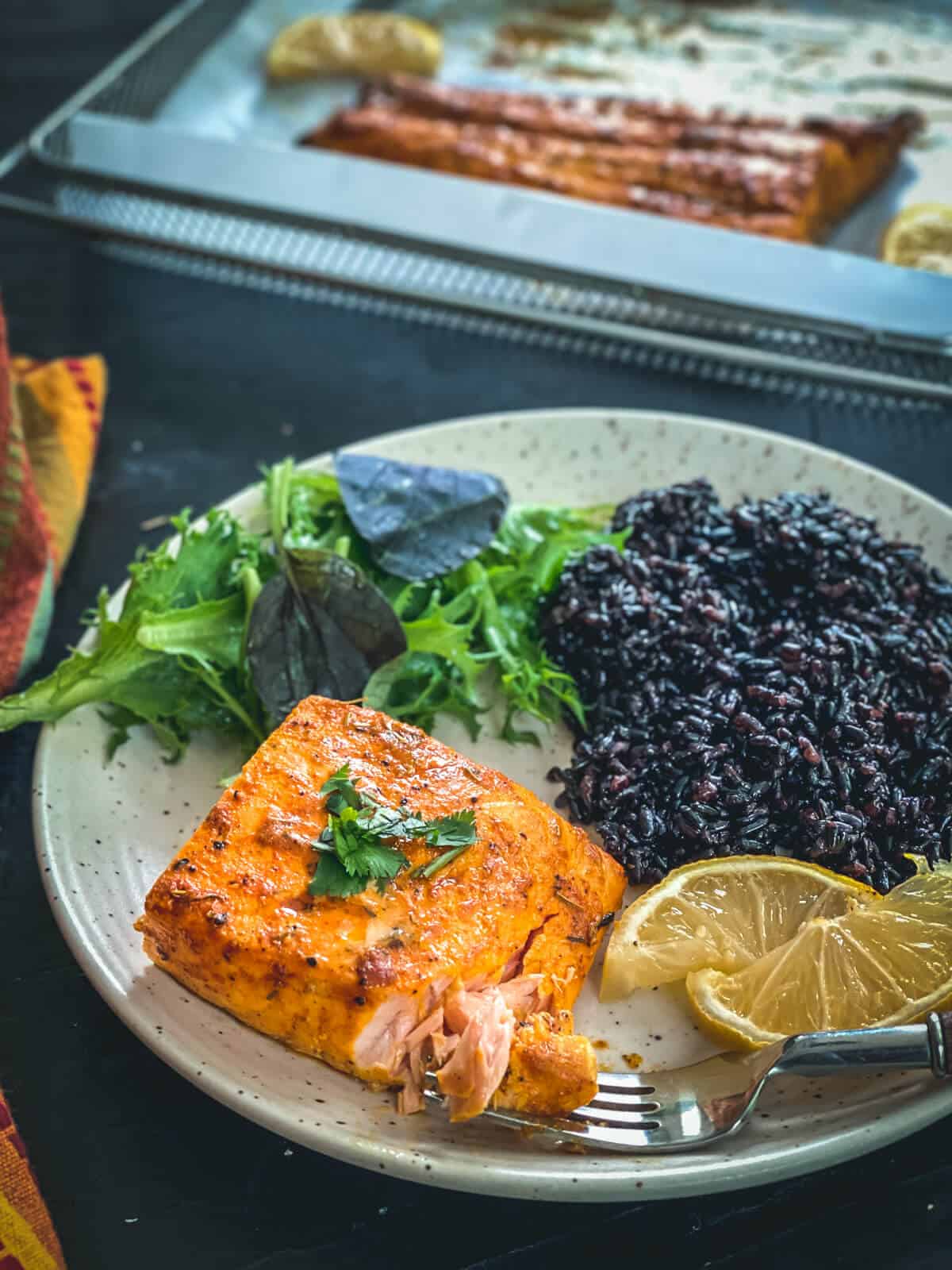 A plate filled with a cooked salmon filet, black rice, and salad on the side.