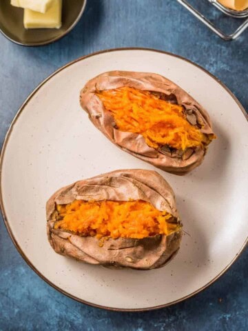A brown rimmed plate with two cut open air fryer sweet potatoes next to a fork.