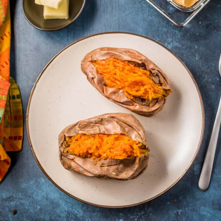 A brown rimmed plate with two cut open air fryer sweet potatoes next to a fork.