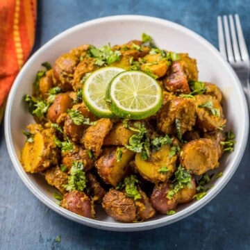 A white bowl with Bombay Potatoes and a silver fork to the right.
