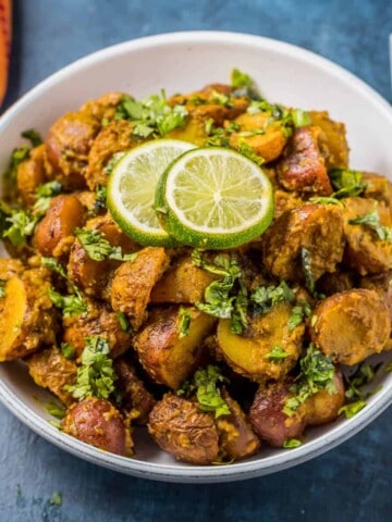 A white bowl with Bombay Potatoes and a silver fork to the right.