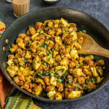 A non-stick skillet with vegetable loaded bread upma and a wooden spoon on the right.