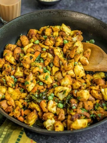 A non-stick skillet with vegetable loaded bread upma and a wooden spoon on the right.