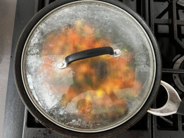 A covered skillet cooking the veggies.